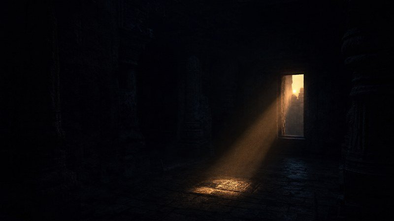 Un raggio di sole che entra dalla porta di un tempio di pietra al buio e disegna un rettangolo di luce sul pavimento